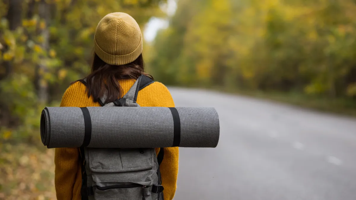 Kobieta na wyprawie z plecakiem i karimatą, korzystająca z akcesoriów turystycznych, które zapewniają komfort podczas biwaku i wyprawy w terenie
