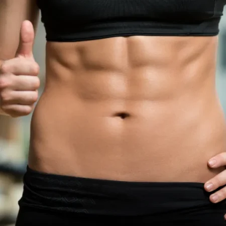 Młoda kobieta prezentuje mięśnie brzucha po ćwiczeniach w domu stosując się do porad z ebooka: 30-dniowa Domowa Rewolucja: Prosty plan na spalanie tłuszczu i budowę formy