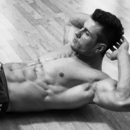 Młody atrakcyjny chłopak prezentuje mięśnie brzucha po domowym treningu